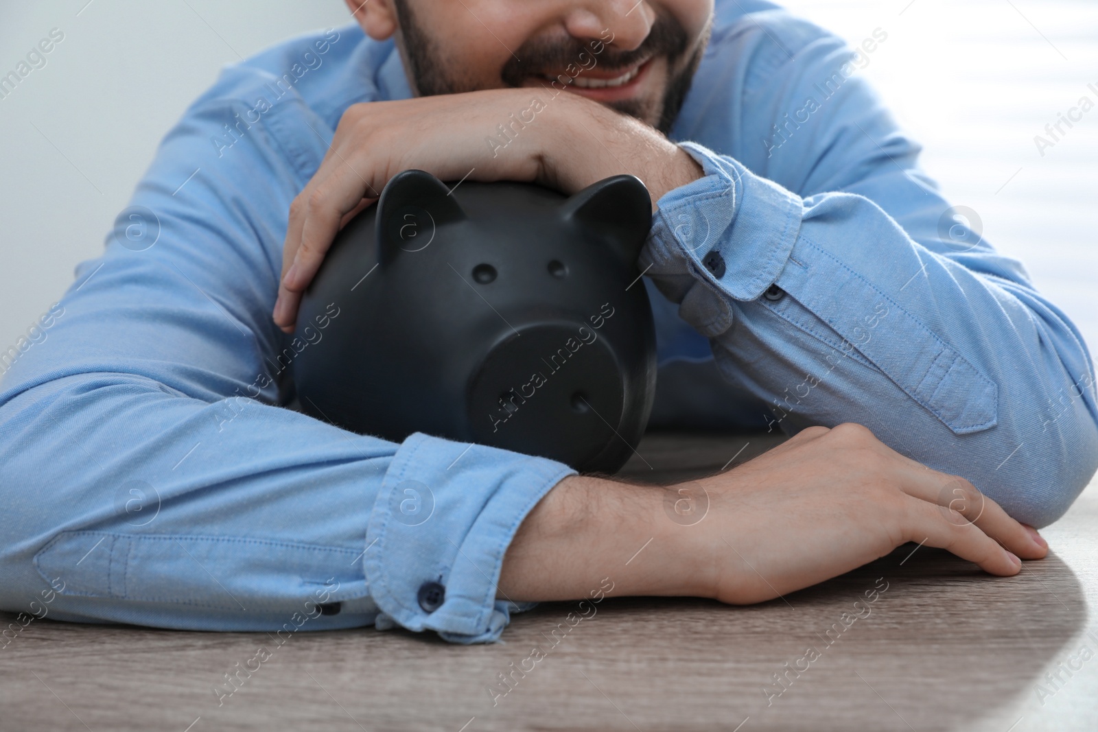 Photo of Man with piggy bank at wooden table, closeup