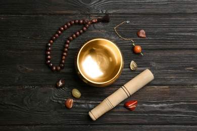 Flat lay composition with golden singing bowl on black wooden table. Sound healing