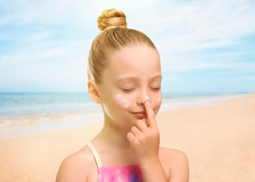 Image of Sun protection. Cute girl applying sunblock onto face on beach