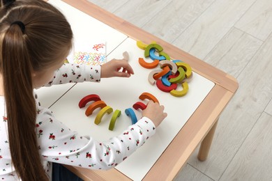 Photo of Motor skills development. Girl playing with colorful wooden arcs at white table indoors, above view