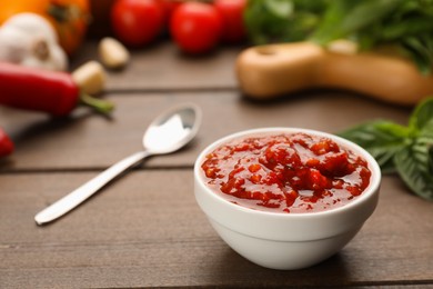 Delicious adjika sauce in bowl and ingredients on wooden table, closeup