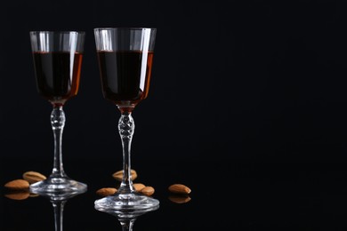 Photo of Liqueur glasses with tasty amaretto and almonds on black table, space for text