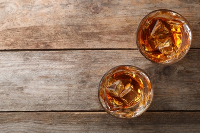 Photo of Golden whiskey in glasses with ice cubes on wooden table, top view. Space for text