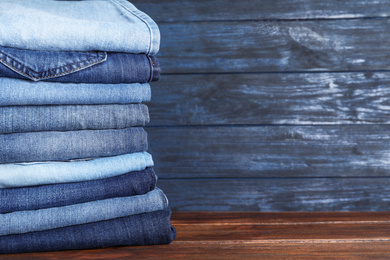 Photo of Stack of different jeans on wooden table, space for text