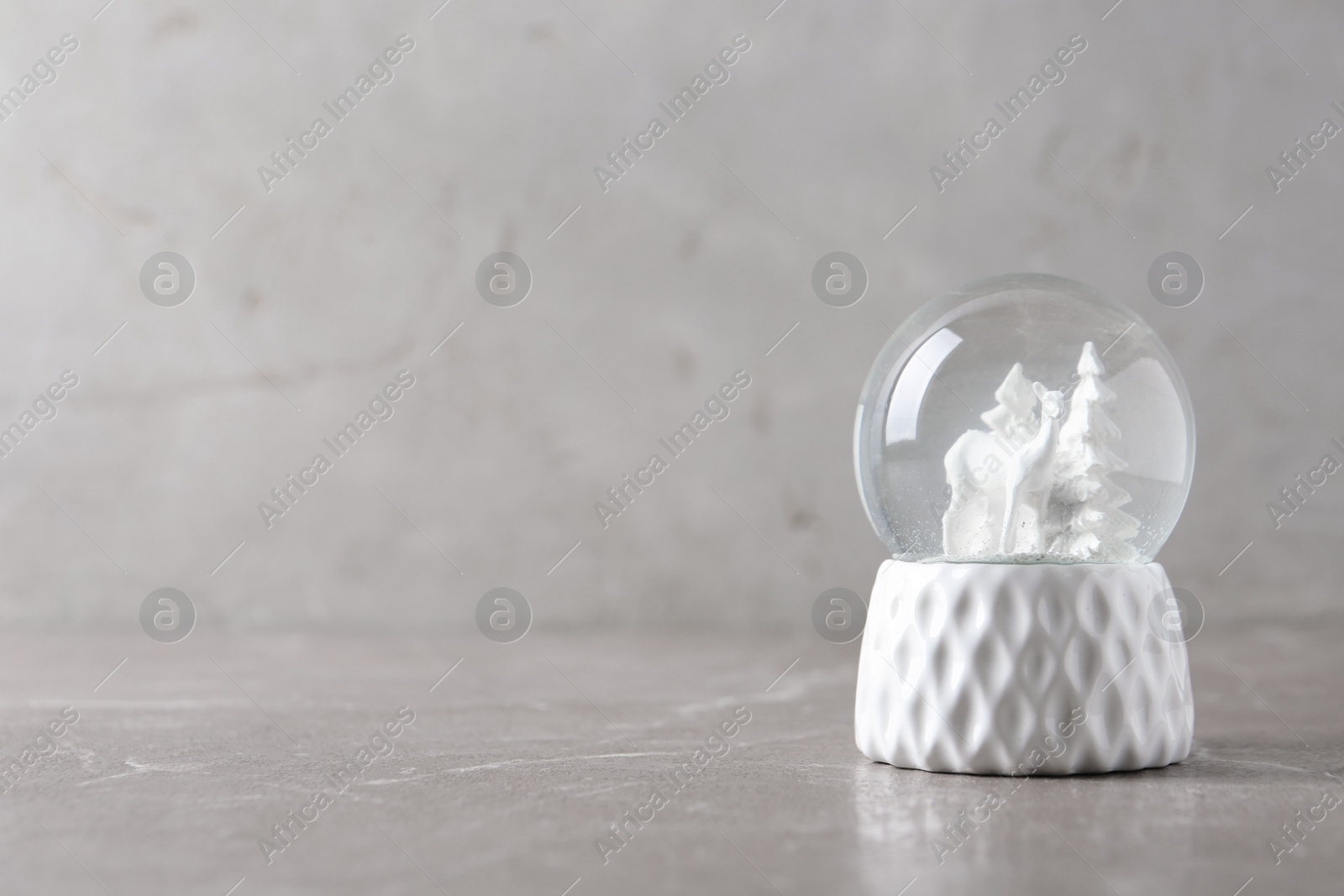Photo of Snow globe with deer and trees on marble table, space for text. Christmas season