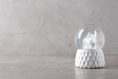 Snow globe with deer and trees on marble table, space for text. Christmas season