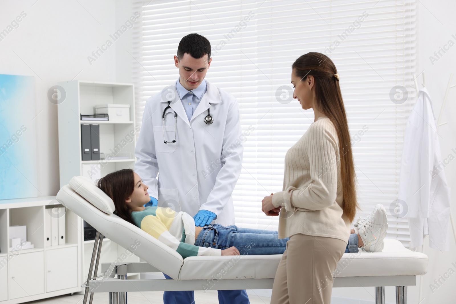 Photo of Gastroenterologist examining girl with stomach ache on couch in clinic