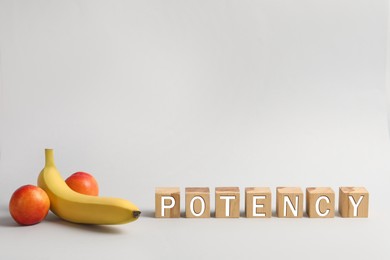 Photo of Cubes with word Potency near banana and nectarines symbolizing male genitals on light grey background, space for text