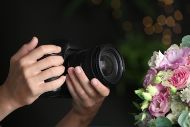 Photo of Young woman holding modern camera near bouquet on dark blurred background, closeup. International Photographer's day