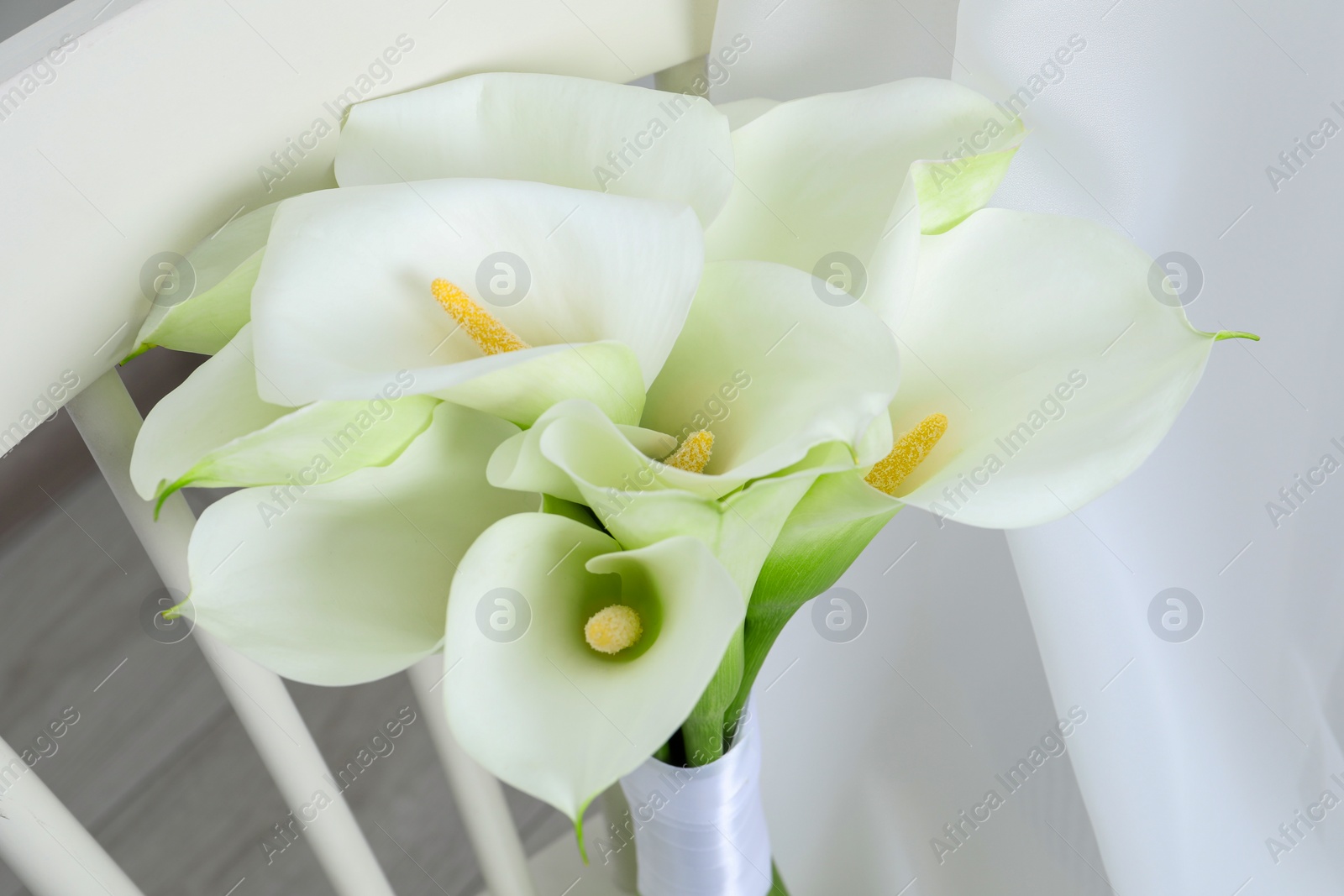 Photo of Beautiful calla lily flowers on white chair indoors, closeup