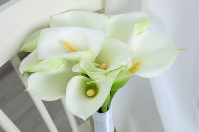 Photo of Beautiful calla lily flowers on white chair indoors, closeup