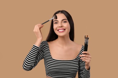 Happy woman with different makeup brushes on light brown background