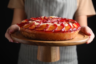 Photo of Woman with delicious plum cake on black background, closeup