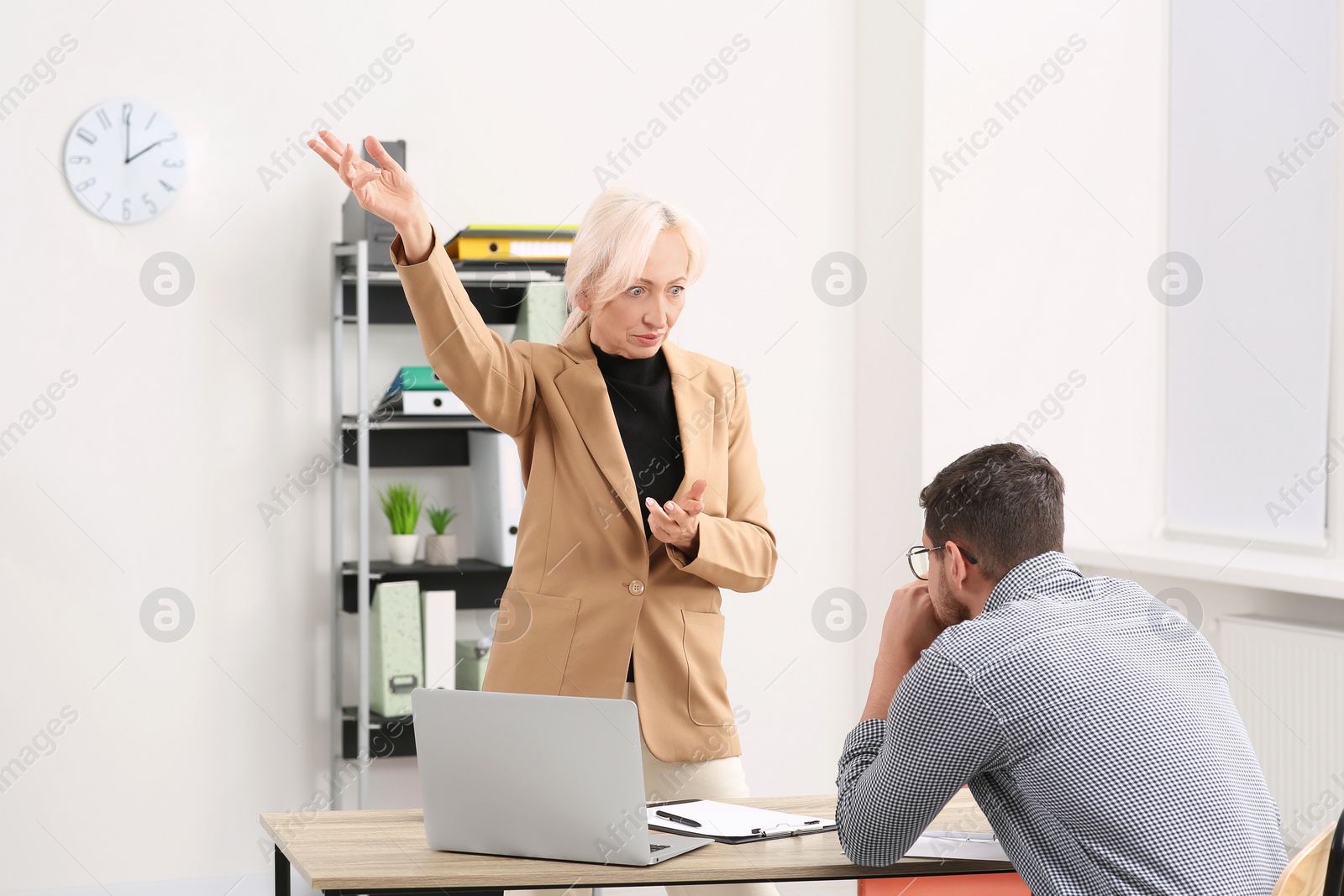 Photo of Emotional boss and stressed employee discussing work issues at wooden table in office