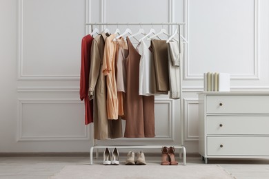 Photo of Rack with different stylish women`s clothes, shoes and chest of drawers near white wall indoors