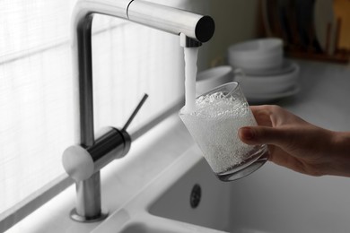 Photo of Woman filling glass with water from tap in kitchen, closeup