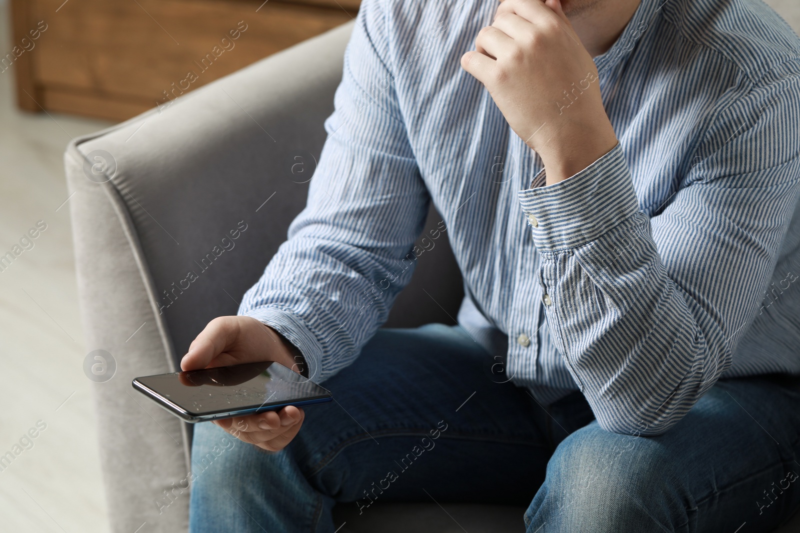 Photo of Man holding damaged smartphone while sitting on armchair indoors, closeup. Device repairing