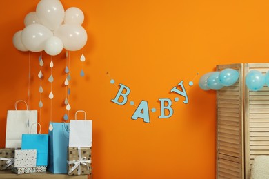 Photo of Baby shower party. Festive decor and gift boxes near orange wall