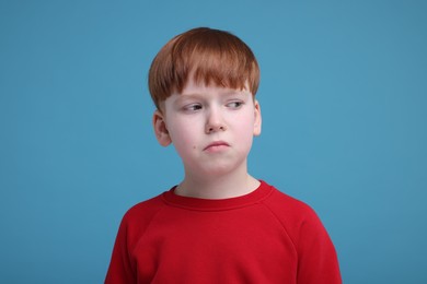 Portrait of sad little boy on light blue background