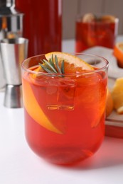 Aperol spritz cocktail, ice cubes, rosemary and orange slices in glass on white wooden table, closeup