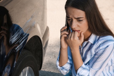 Photo of Stressed woman talking on phone near car with scratch outdoors, closeup