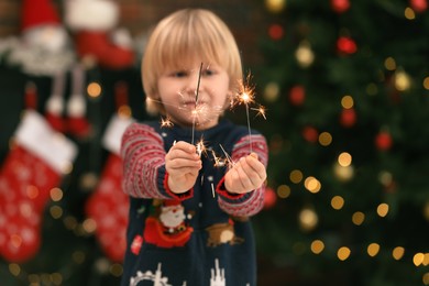 Photo of Little child with burning sparklers at home, selective focus. Christmas celebration
