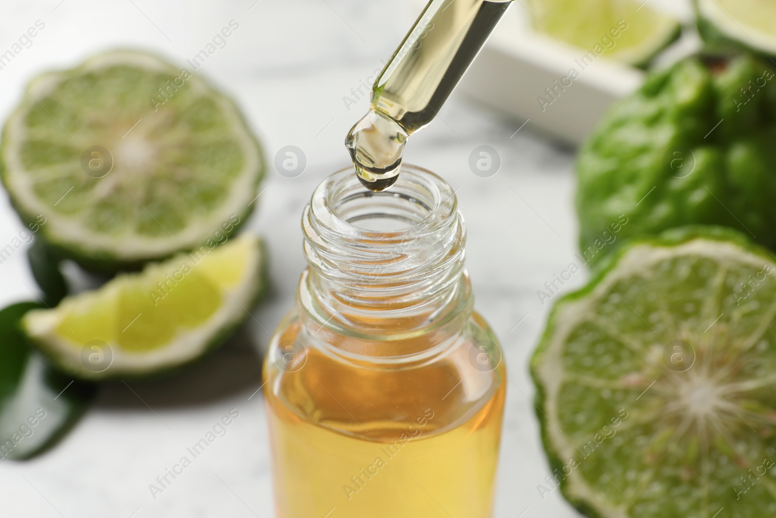 Photo of Bergamot essential oil dripping from pipette into bottle on table, closeup