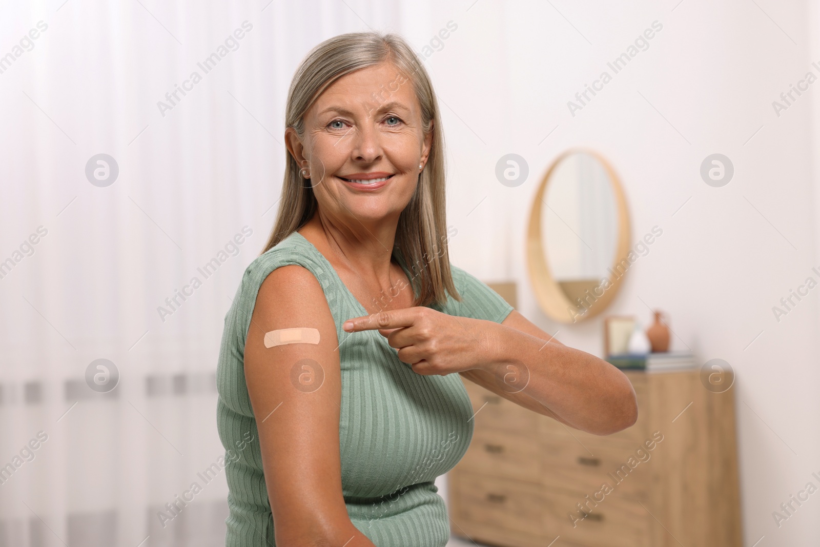 Photo of Senior woman pointing at adhesive bandage after vaccination in room