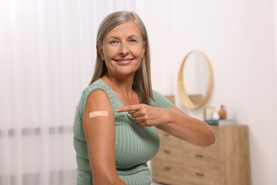 Senior woman pointing at adhesive bandage after vaccination in room