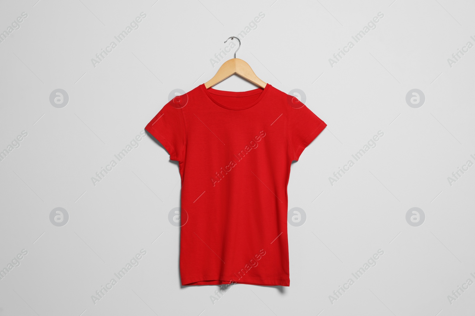 Photo of Hanger with red t-shirt on light wall. Mockup for design