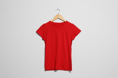 Photo of Hanger with red t-shirt on light wall. Mockup for design