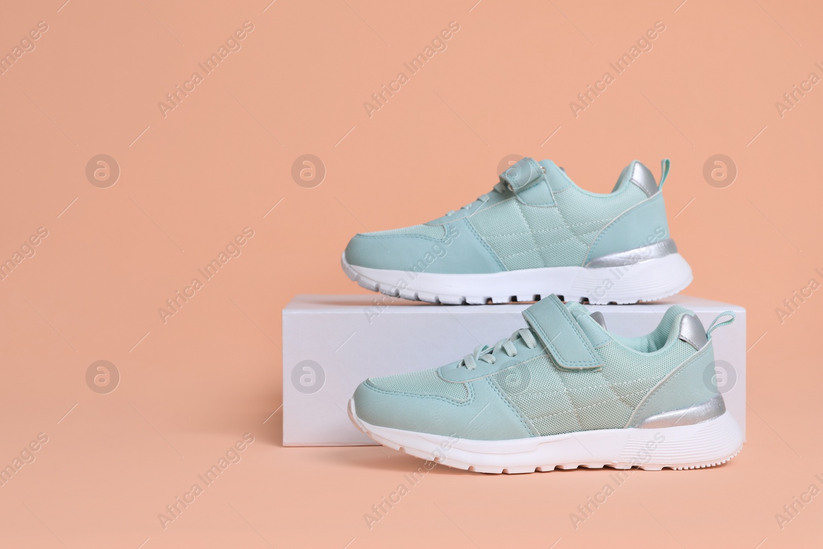 Photo of Pair of comfortable sports shoes and box on pale coral background. Space for text