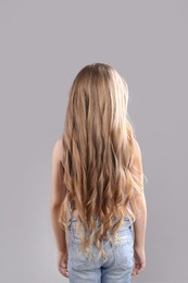 Photo of Little girl with wavy hair on grey background, back view