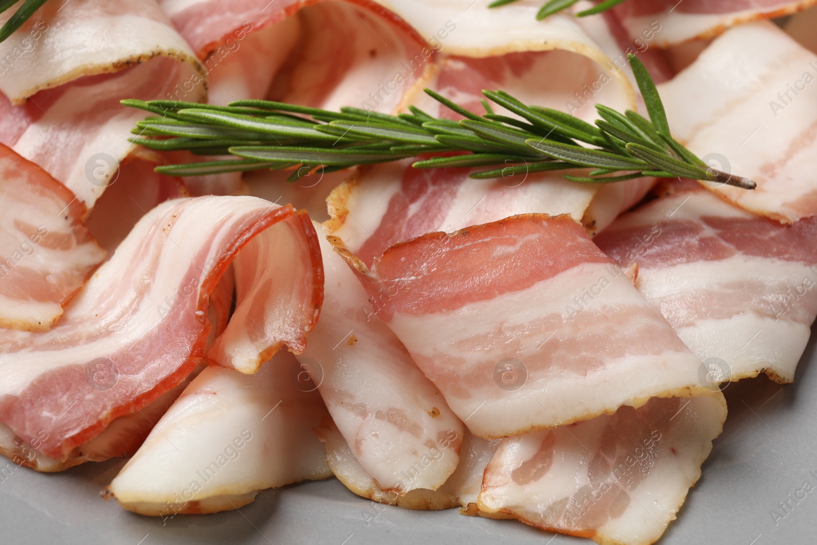 Photo of Slices of raw bacon and rosemary on gray table, closeup