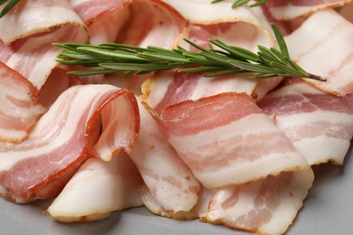 Slices of raw bacon and rosemary on gray table, closeup