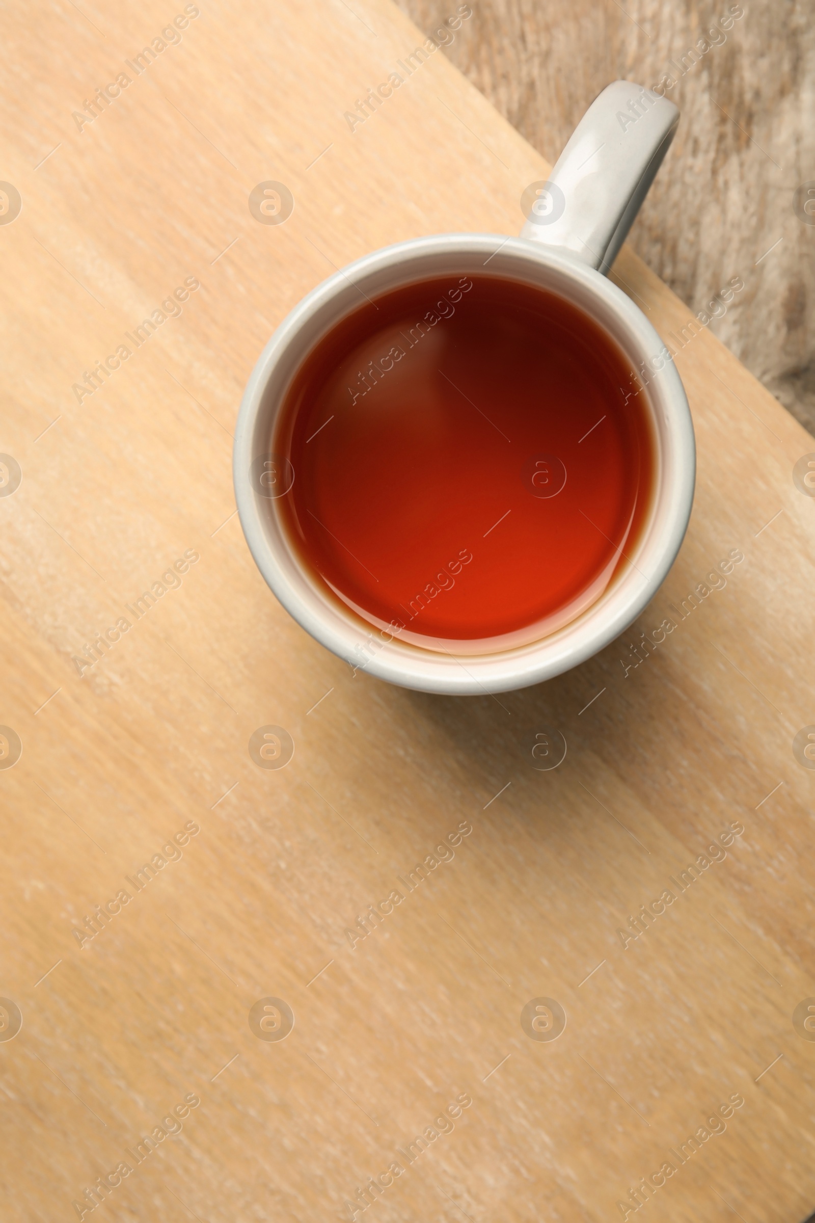 Photo of Cup of black tea on wooden board, top view