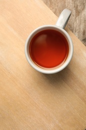 Photo of Cup of black tea on wooden board, top view