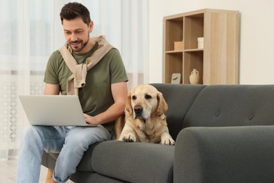Man using laptop on sofa near his cute Labrador Retriever at home. Space for text