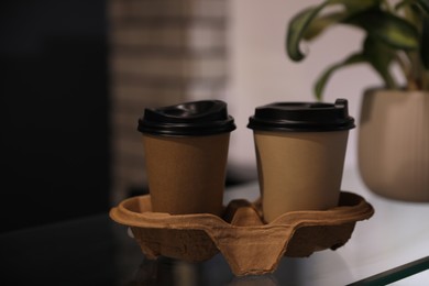 Photo of Takeaway coffee cups with cardboard holder on glass table in cafe