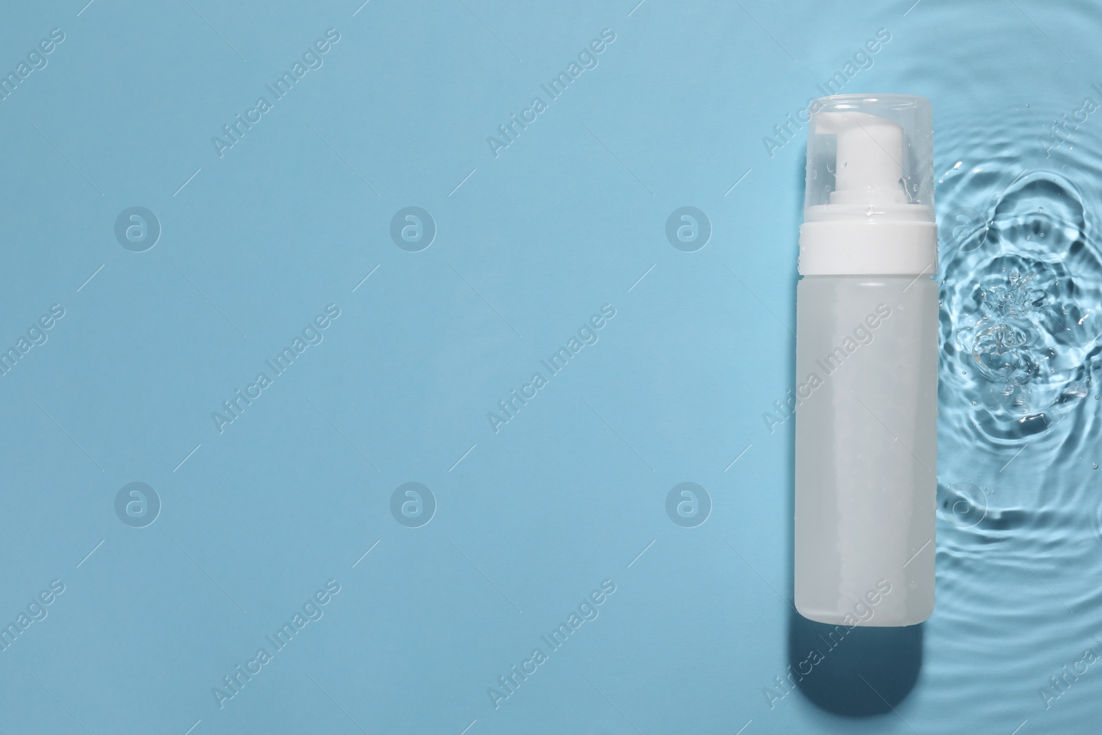 Photo of Bottle of face cleansing product in water against light blue background, top view. Space for text