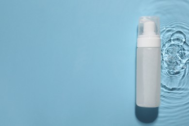 Photo of Bottle of face cleansing product in water against light blue background, top view. Space for text