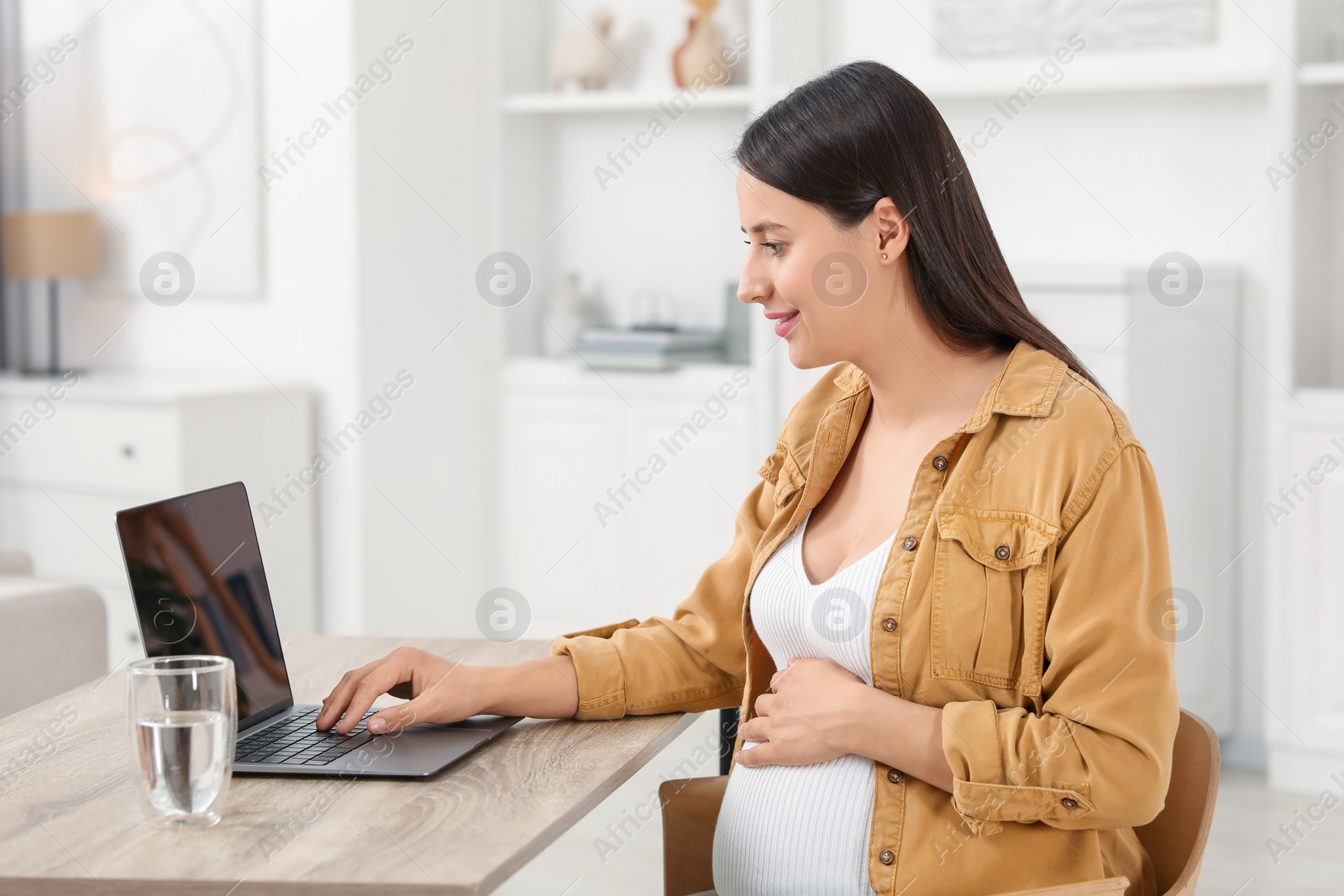 Photo of Beautiful pregnant woman using laptop at wooden table in room