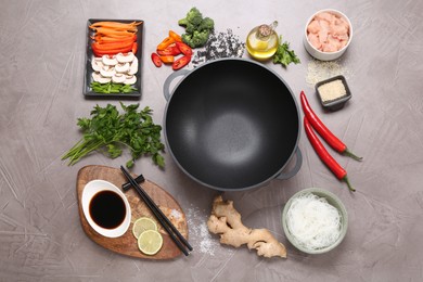 Photo of Wok, chopsticks and different products on grey textured table, flat lay