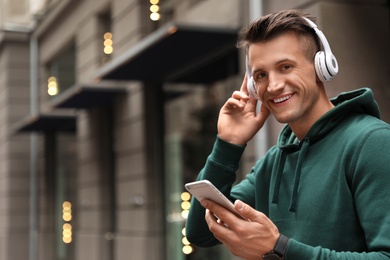 Photo of Portrait of handsome man with headphones and smartphone listening to music on city street. Space for text