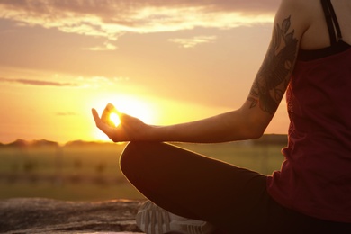Photo of Young woman practicing zen yoga at sunrise outdoors, closeup