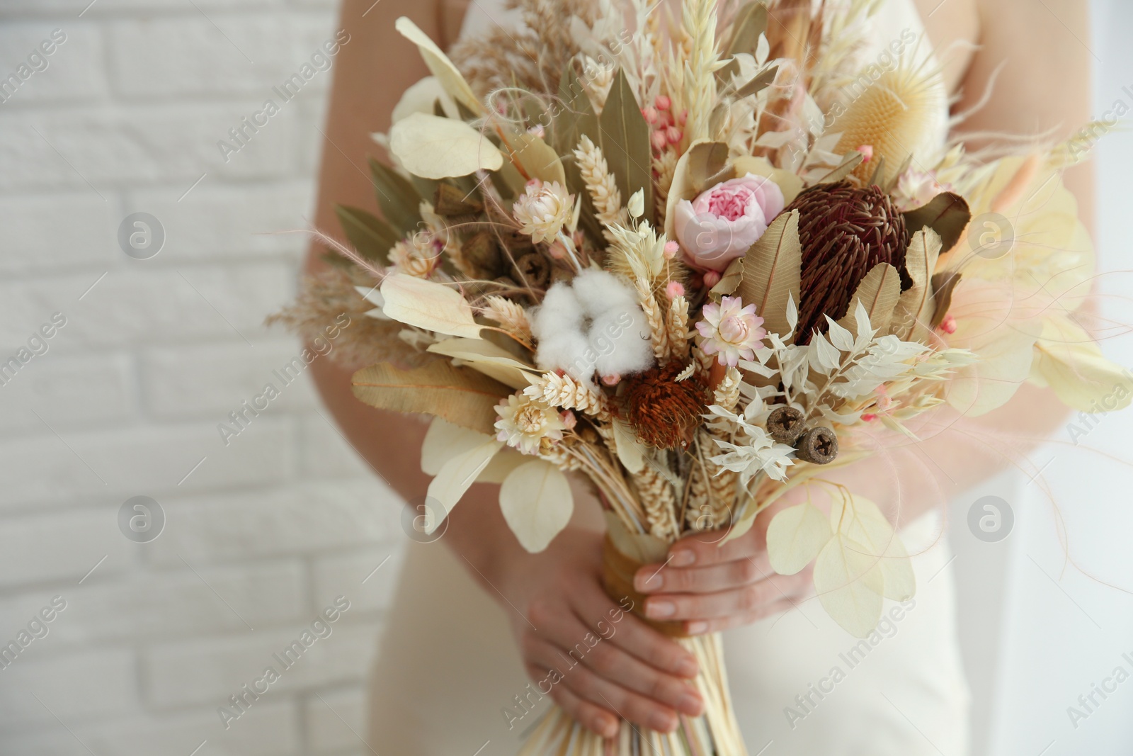 Photo of Bride holding beautiful dried flower bouquet at home, closeup