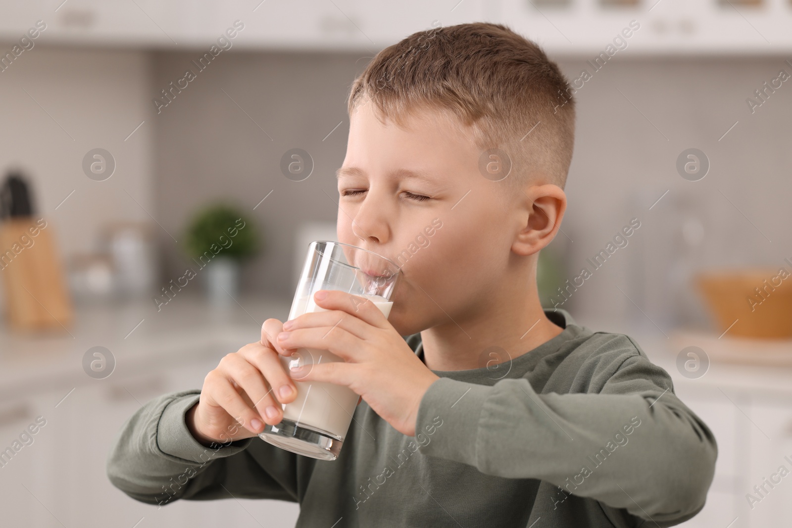 Photo of Cute boy drinking fresh milk from glass indoors