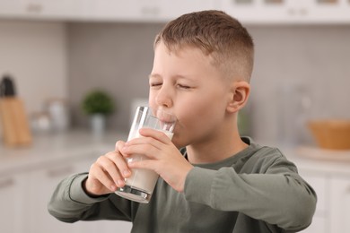 Cute boy drinking fresh milk from glass indoors