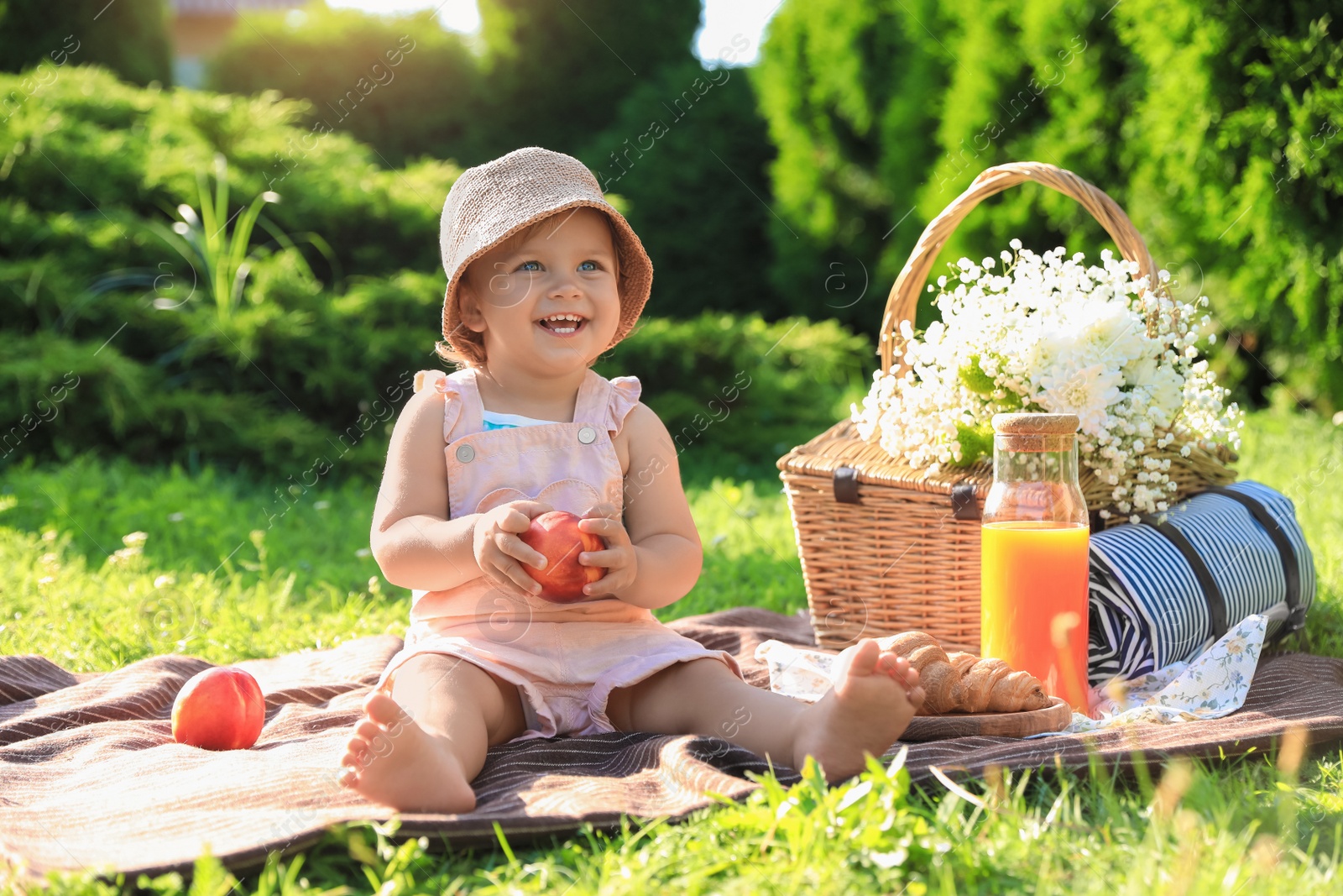 Photo of Cute little baby girl with nectarine on picnic blanket in garden