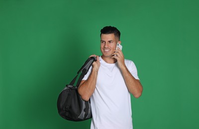 Photo of Handsome man with sports bag and smartphone on green background